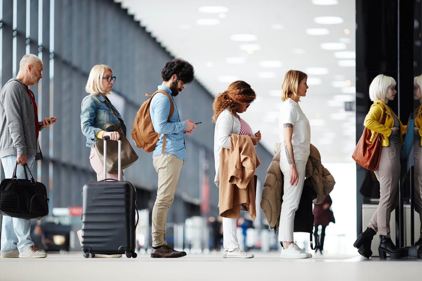 Side view of multiracial people standing in queue to check in in airport hall. They are holding various types of luggage and outerwear
