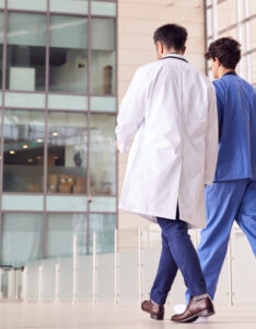 Two healthcare workers walking away, one wearing a white coat and one in blue scrubs