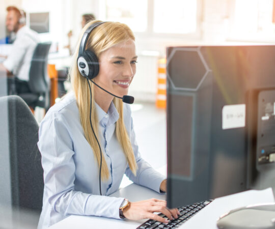 Woman sitting a desk in an an office. Working at a desktop computer, wearing a headset