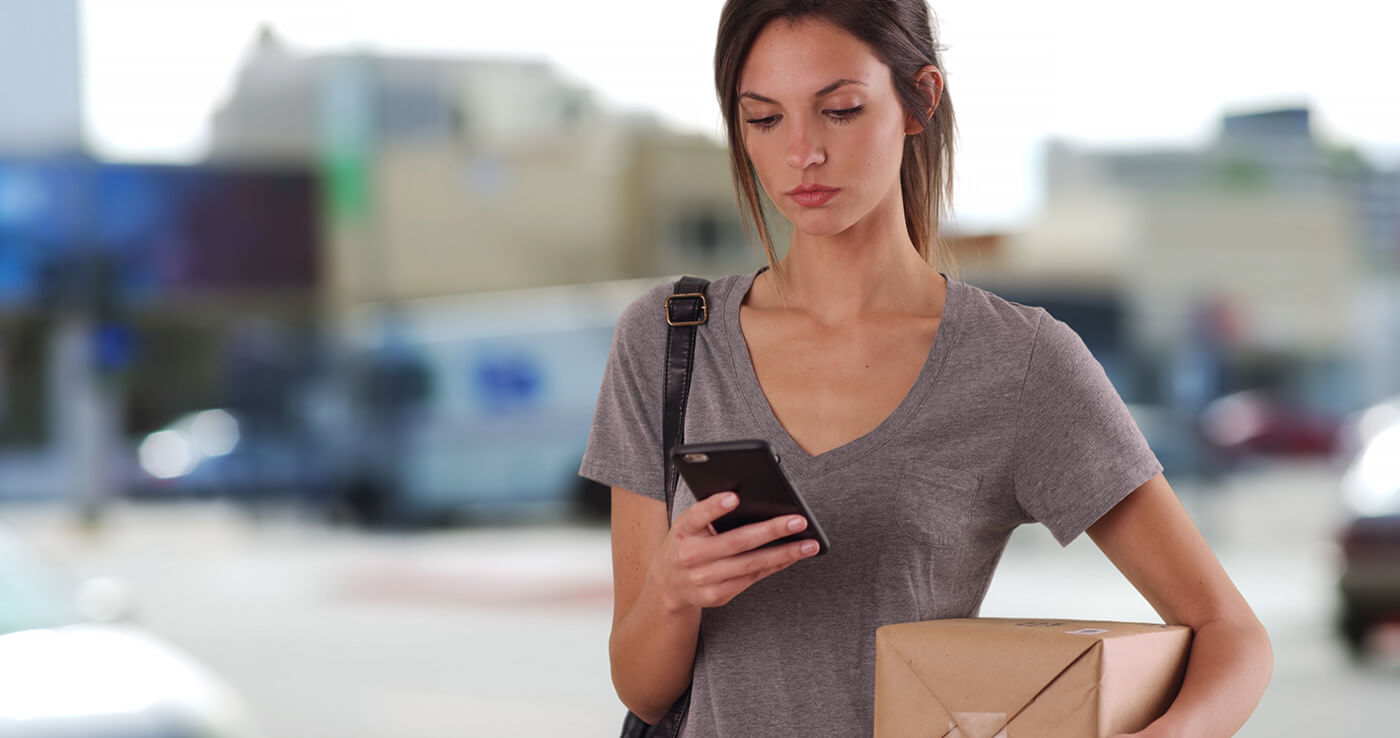 female using smartphone while carrying a package