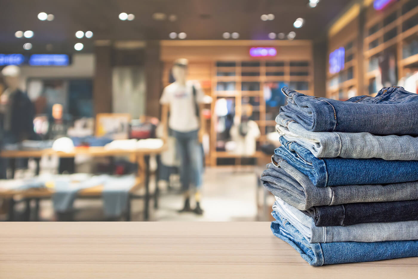 stack of denim jeans on a counter with blurred store in background