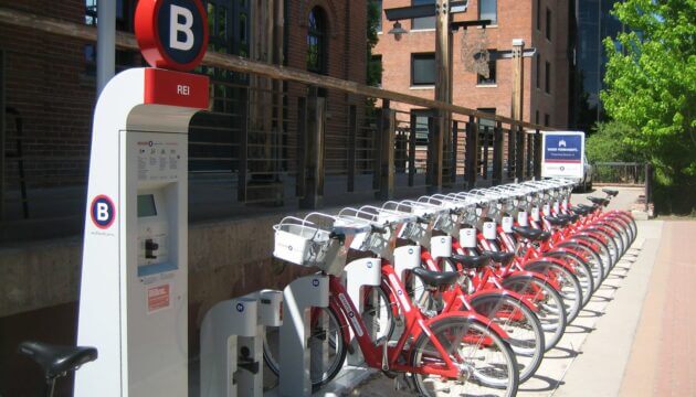 A row of red rental bikes, attached to a payment kiosk