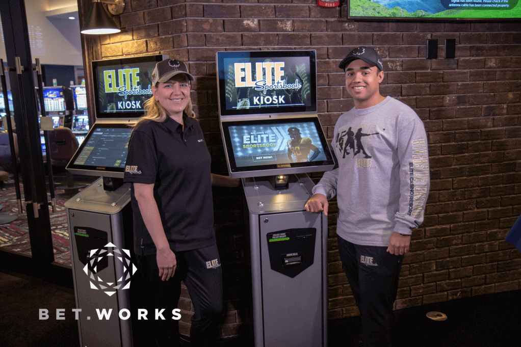 elite sportsbook kiosk with two reps posing beside it