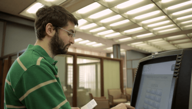 Man in green shirt and glasses using a bill payment kiosk