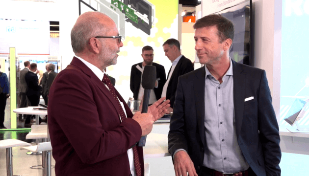 A man in a red suit interviewing another well dressed man