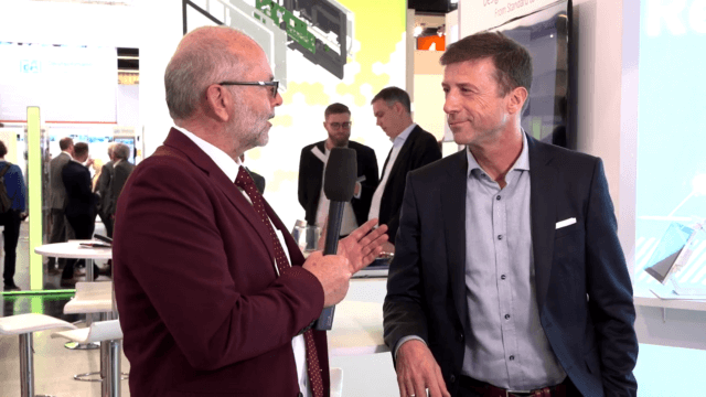 A man in a red suit interviewing another well dressed man