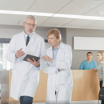 Man and woman in lab coats, walking in a hospital while looking at a chart