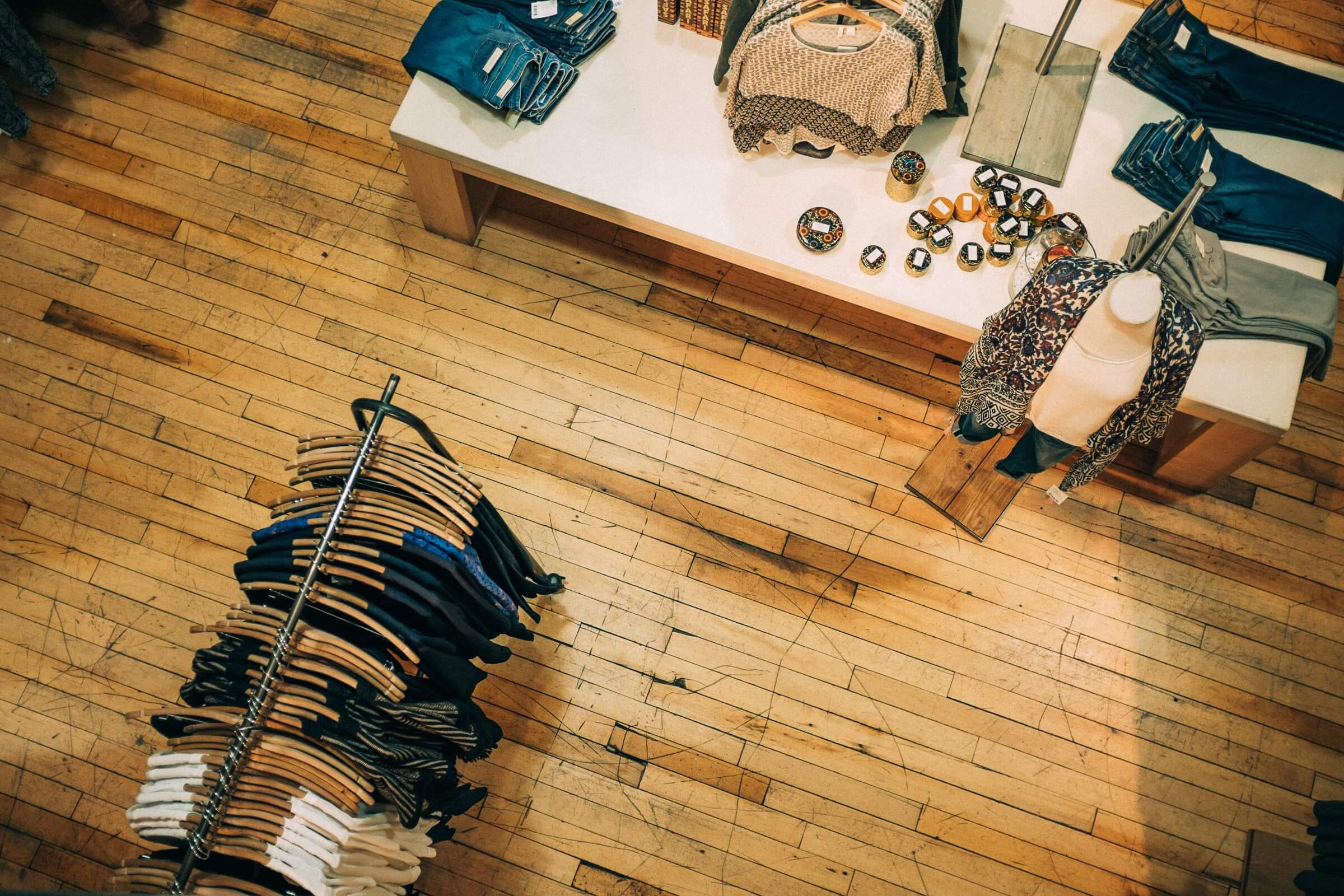 A retail store seen from above. A rack of clothes stand on a wood panel floor.