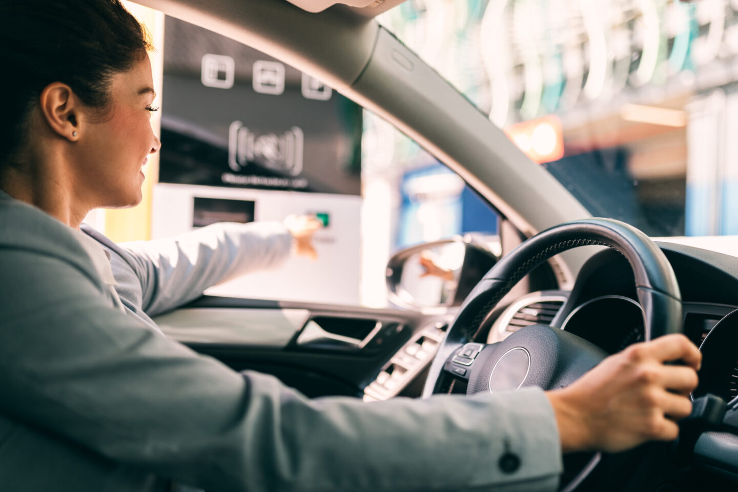A woman reaches from her car to tap a button on a parking kiosk, enjoying a fast, hassle-free experience.