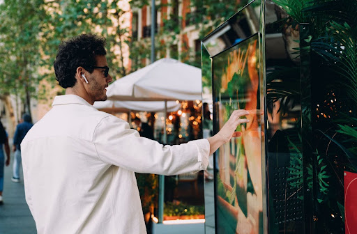 Man interacting with outdoor touchscreen kiosk displaying digital signage content on a city street.